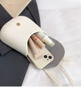 Detail showing internal capacity of white leather crossbody bag with phone and lipstick