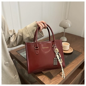 Detail of burgundy leather tote bag featuring fashion text and chocolate charm pendant