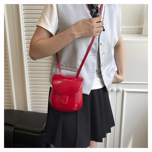 Detail of red vintage horseshoe crossbody bag styled with a grey vest and black pleated skirt