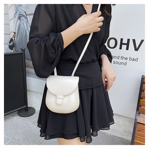 Detail view of a cream white mini saddle bag in glossy leather worn by a model