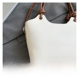 Detail of white bucket bag with brown knotted handle and silver-tone metal hardware