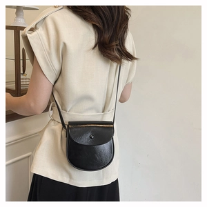Detailed side view of a black glossy leather saddle bag worn by a model in soft lighting