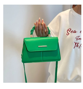 Détail du sac bandoulière vert avec poignée tressée et boucle métallique sur fond blanc