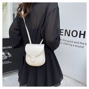 Detail view of a cream white horseshoe saddle bag worn over a black dress with strap