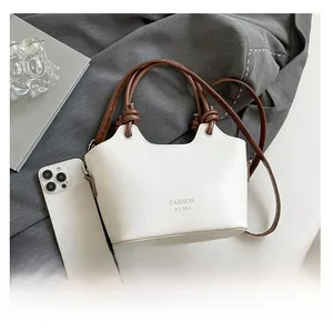 Detail view of white bucket bag with brown handles and Fashion H.C Bag logo on grey suit