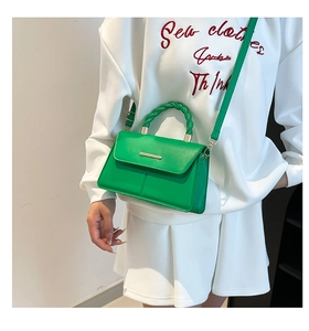 Detail of a bright green crossbody bag featuring a twisted handle and gold metal accents