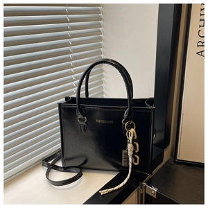 Détail du sac cabas noir brillant avec lettrage doré et pendentif sur le rebord de fenêtre