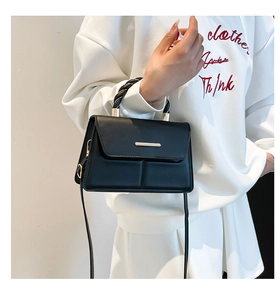 Détail d'un sac à main carré en cuir noir avec bordure dorée et coutures croisées