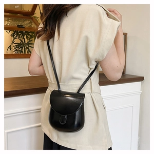 Close-up of the glossy black mini horseshoe bag worn on a shoulder in a cozy interior