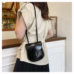 Close-up of black glossy crossbody bag with minimalist flap design and shoulder strap