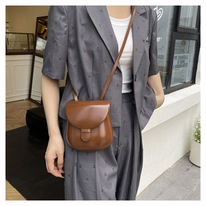 Close-up of a brown glossy leather crossbody bag worn with a charcoal gray blazer
