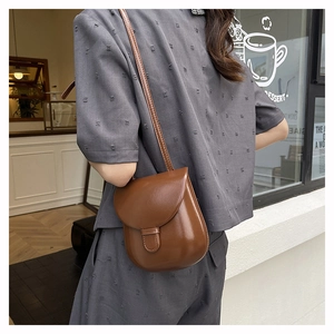 Side view of a vintage brown saddle bag worn by a model in a bright, modern cafe setting