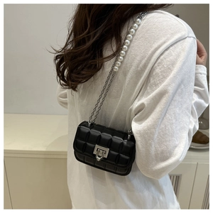 Detail of a black quilted crossbody bag with a pearl and silver metal chain strap