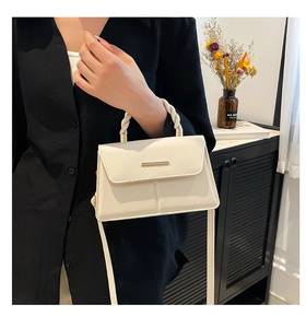 Detail of cream leather handbag featuring a unique woven handle and gold metal bar accent