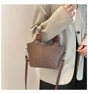 Brown leather bucket bag with knot handle and shoulder strap worn with grey suit