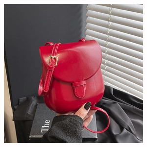 Detail of red PU leather saddle bag with glossy finish and gold metal buckle strap