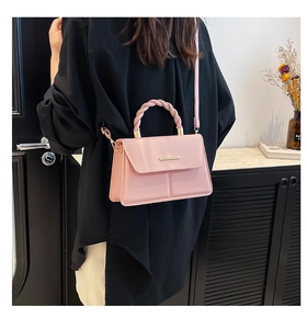 Détail du sac à main en cuir verni rose avec poignée tressée et boucle dorée sur marbre