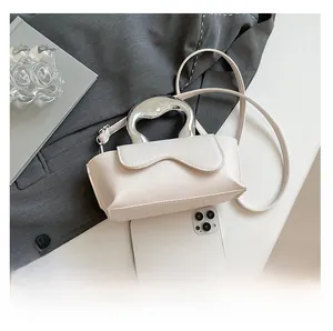 Close-up of cream handbag with fluid silver handle next to a phone for size comparison