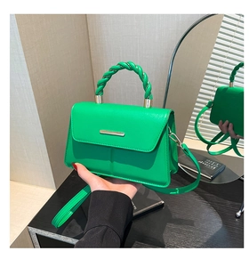 Detail of green crossbody bag with woven handle and gold metal clasp closure