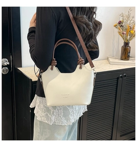 Detail of minimalist cream bucket bag with brown handles and adjustable shoulder strap