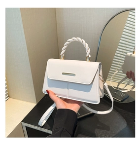 Detail of white leather handbag featuring twisted handle and gold metal bar decoration