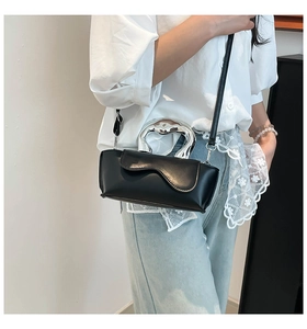 Detail of minimalist black leather crossbody bag featuring an artistic silver metal handle