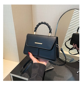 Detail of a black leather handbag featuring a unique braided handle and gold metal hardware