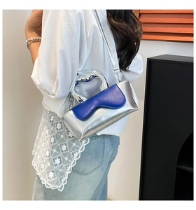Close-up of the silver heart-shaped metal handle and blue leather flap of the handbag