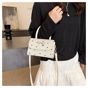 Sac à bandoulière crème avec nœuds, texture plissée et boucle argentée sur mannequin