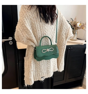 Detailed view of crocodile pattern emerald green handbag with a large rhinestone bow