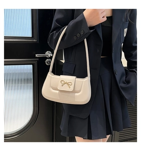 Détail d'un sac baguette crème avec nœud doré porté sur une veste de tailleur bleu marine