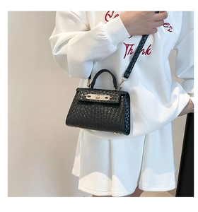 Detail of black woven texture handbag with golden metal twist lock shown on a model