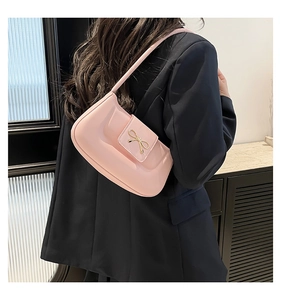Détail du sac à bandoulière rose clair avec un nœud décoratif doré en métal sur cuir lisse