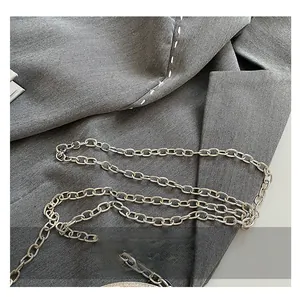 Detail of a shiny silver metal chain strap on a textured grey blazer fabric background