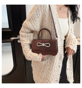 Detail of brown crocodile pattern leather handbag with crystal bow and wavy flap
