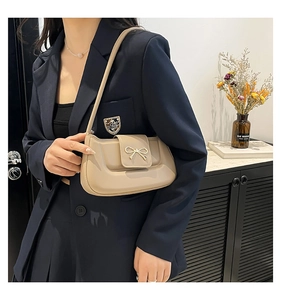 Detail of a beige crescent bag with a gold bow clasp worn with a navy suit jacket