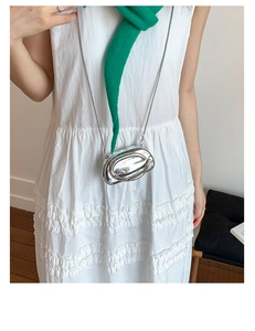 Mini silver mirror handbag with oval metal logo and chain strap worn by a model