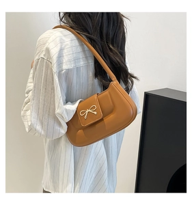 Détail du sac croissant camel avec boucle nœud doré porté à l'épaule du modèle