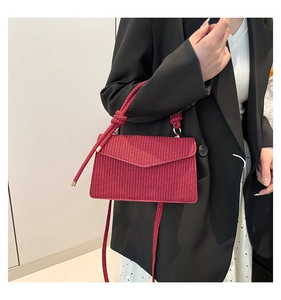 Detail view of deep red woven crossbody bag featuring a textured flap and top handle
