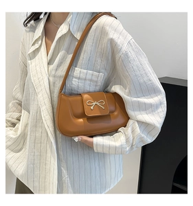 Detail of tan faux leather shoulder bag with a silver bow clasp on a white shirt