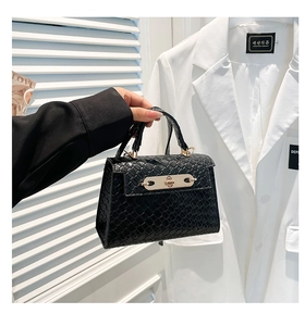 Detail of black crocodile embossed faux leather handbag with gold metal lock closure