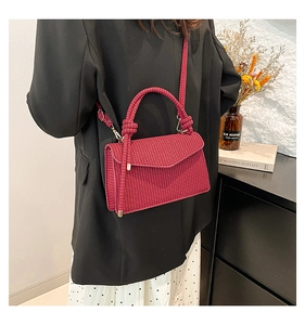 Detail of a dark red woven crossbody bag featuring a textured finish and strap