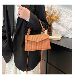 Detailed texture of brown straw crossbody bag held by a model in casual chic outfit