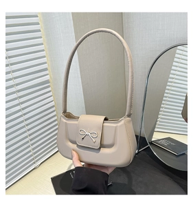 Detailed view of silver metal bow accent on chic beige faux leather shoulder bag