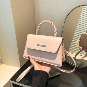 Sac bandoulière rose avec poignée torsadée et boucle dorée tenu en main