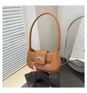 Detail of caramel leather shoulder bag featuring a silver metal bow buckle accent