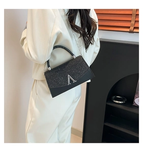 Detail of black crossbody bag with glitter flap and silver V-clasp on white blazer