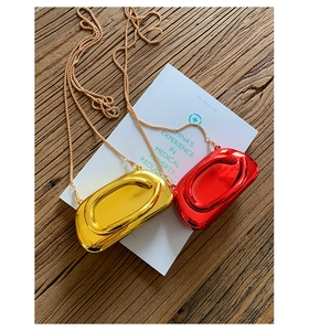 Detail view of mini metallic chain bags in shiny gold and red with mirror finish surface