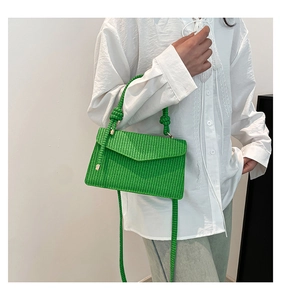 Detail of bright green woven texture shoulder bag with knotted handle on white shirt