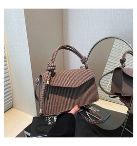 Detail of a brown woven leather crossbody bag with a triangular flap and a knotted top handle
